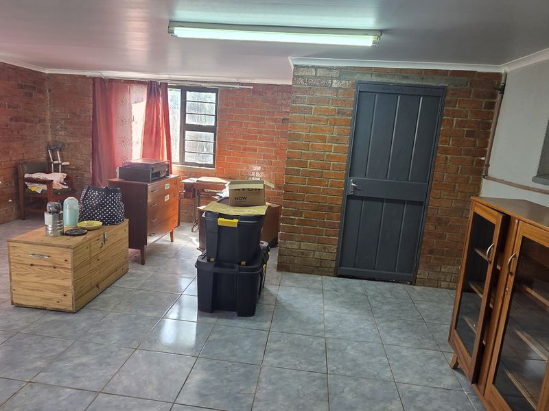 A spacious living area featuring exposed brick walls, ceramic tile flooring, and large windows with security bars, offering a blank canvas for renovation.