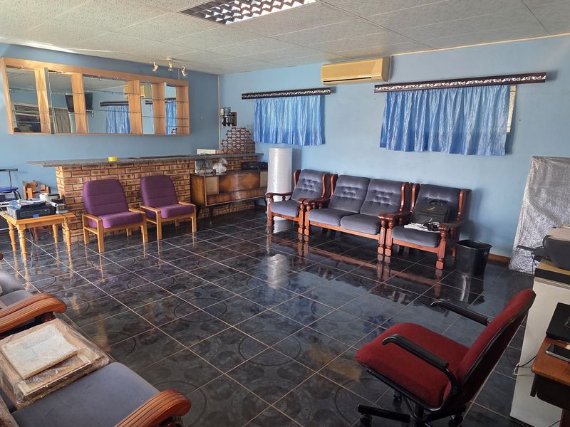 Spacious living area featuring dark tiled flooring, a built-in brick bar, and wall-mounted air conditioning, offering a functional layout with potential for modernization.