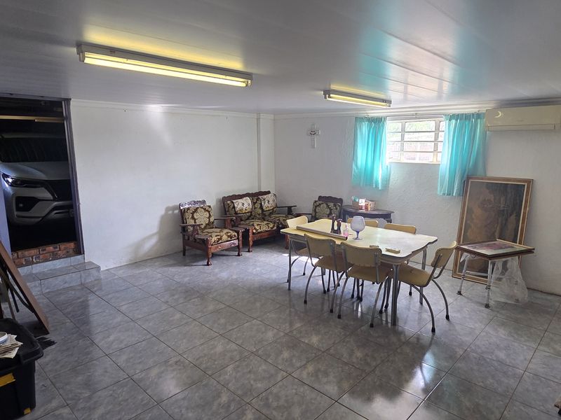 An open-plan living and dining area featuring tiled flooring, fluorescent lighting, and a wall-mounted air conditioning unit.