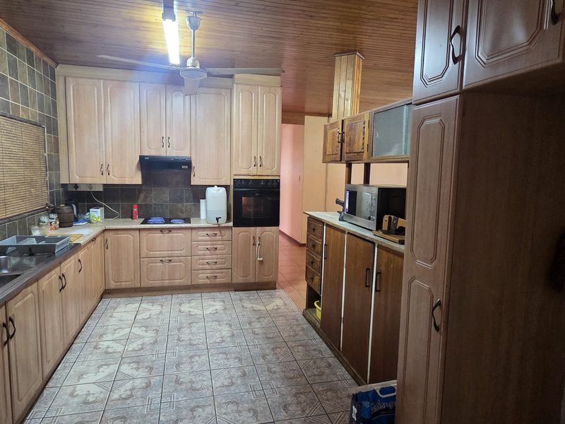 A functional kitchen featuring extensive wooden cabinetry, built-in oven and hob, tiled splashbacks, and a timber-clad ceiling, offering a traditional aesthetic.