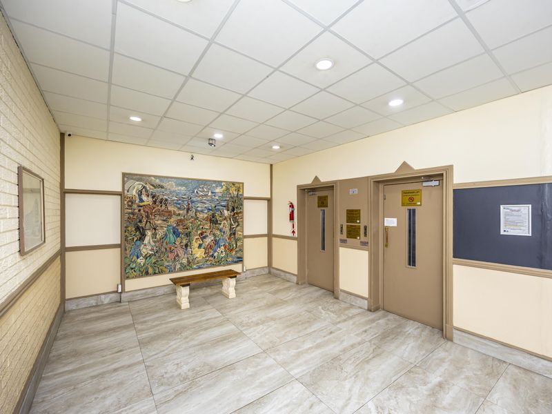 A clean and well-maintained apartment building lobby featuring tiled flooring, recessed lighting, and dual passenger lift access.