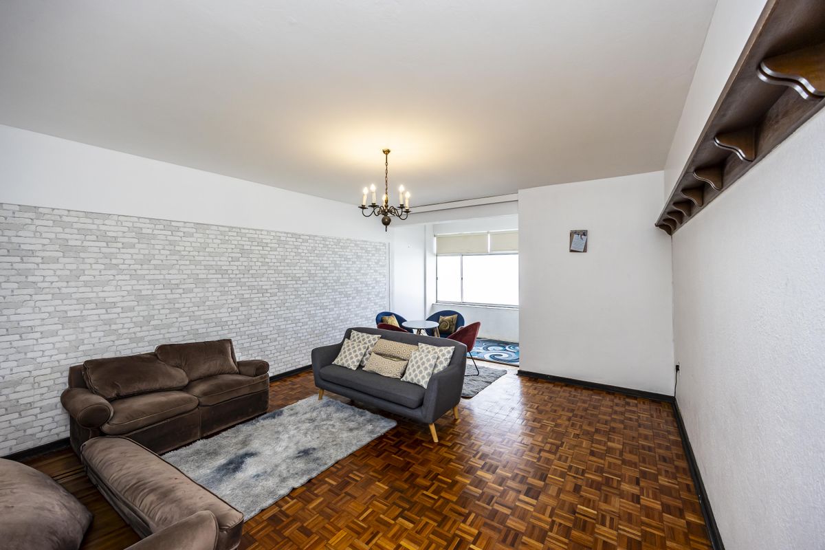 Spacious living room featuring classic parquet flooring, a decorative brick-effect feature wall, and a traditional chandelier, offering a bright and versatile living space.