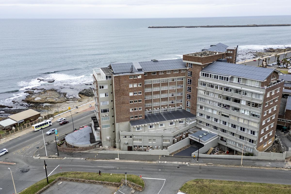 Aerial view of a multi-story apartment building featuring a brick facade and rooftop solar panels, situated along the coastline.
