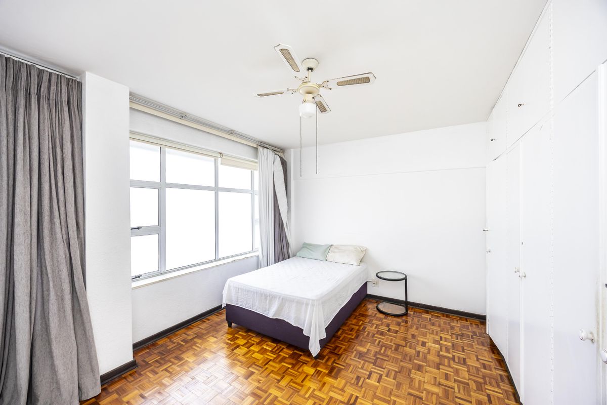 A bright bedroom featuring classic parquet flooring, a ceiling fan, and ample built-in cupboard storage space.