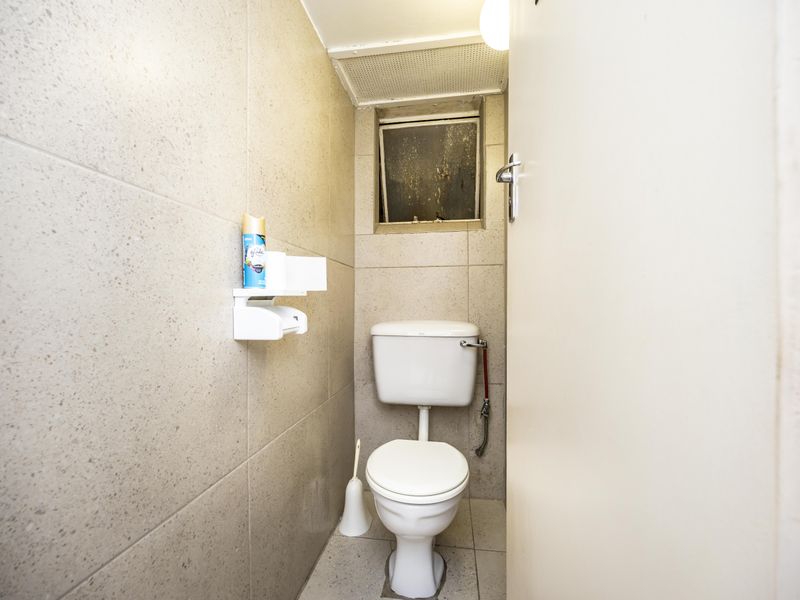 A compact, tiled guest toilet featuring a standard white toilet suite and a small ventilation window.