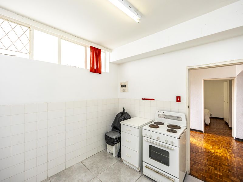 A functional kitchen area featuring a freestanding electric stove, tiled splashbacks, and parquet flooring, leading into an adjacent room.