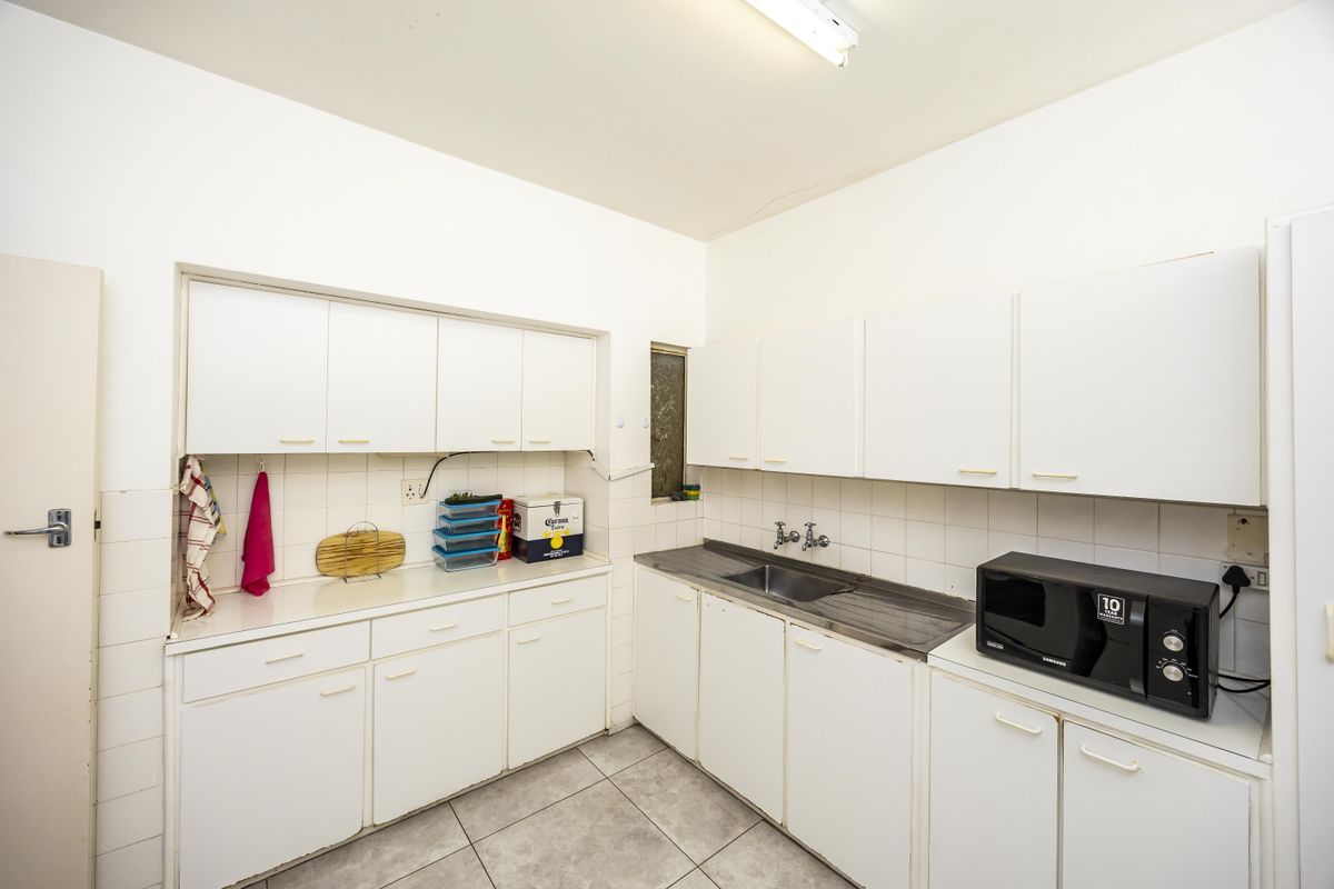 A functional kitchen featuring white cabinetry, tiled backsplash, and stainless steel sink, offering a blank canvas for potential modern updates.