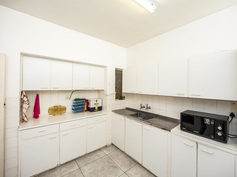A functional kitchen featuring white cabinetry, tiled backsplash, and stainless steel sink, offering a blank canvas for potential modern updates.