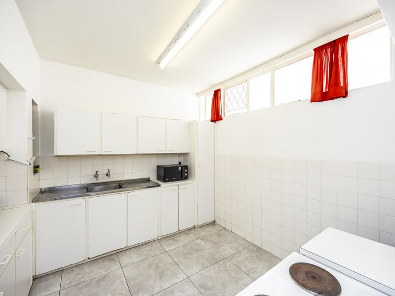 A functional laundry room featuring built-in white cabinetry, a stainless steel sink, tiled splashbacks, and durable floor tiles with high-level windows for natural light.