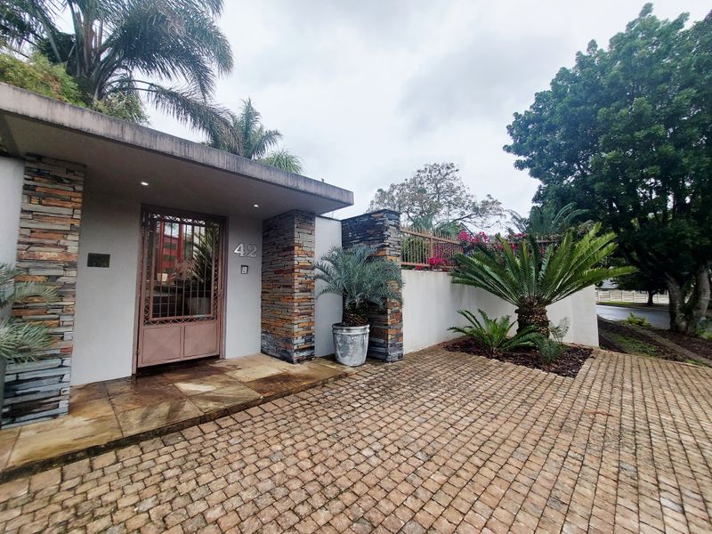 Front entrance featuring stone cladding, a secure metal gate, and a cobblestone driveway with established landscaping.