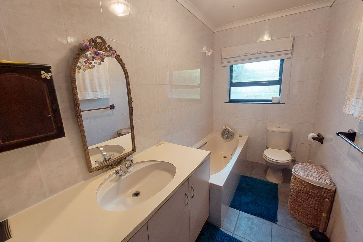 A functional bathroom featuring a built-in vanity with inset basin, a bathtub, and a toilet, finished with neutral wall and floor tiling.