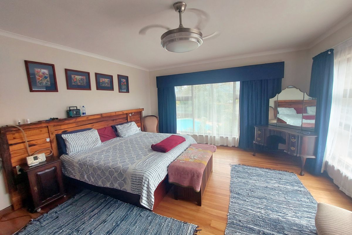 Spacious bedroom featuring hardwood flooring, a ceiling fan, and large windows with views of the pool area.