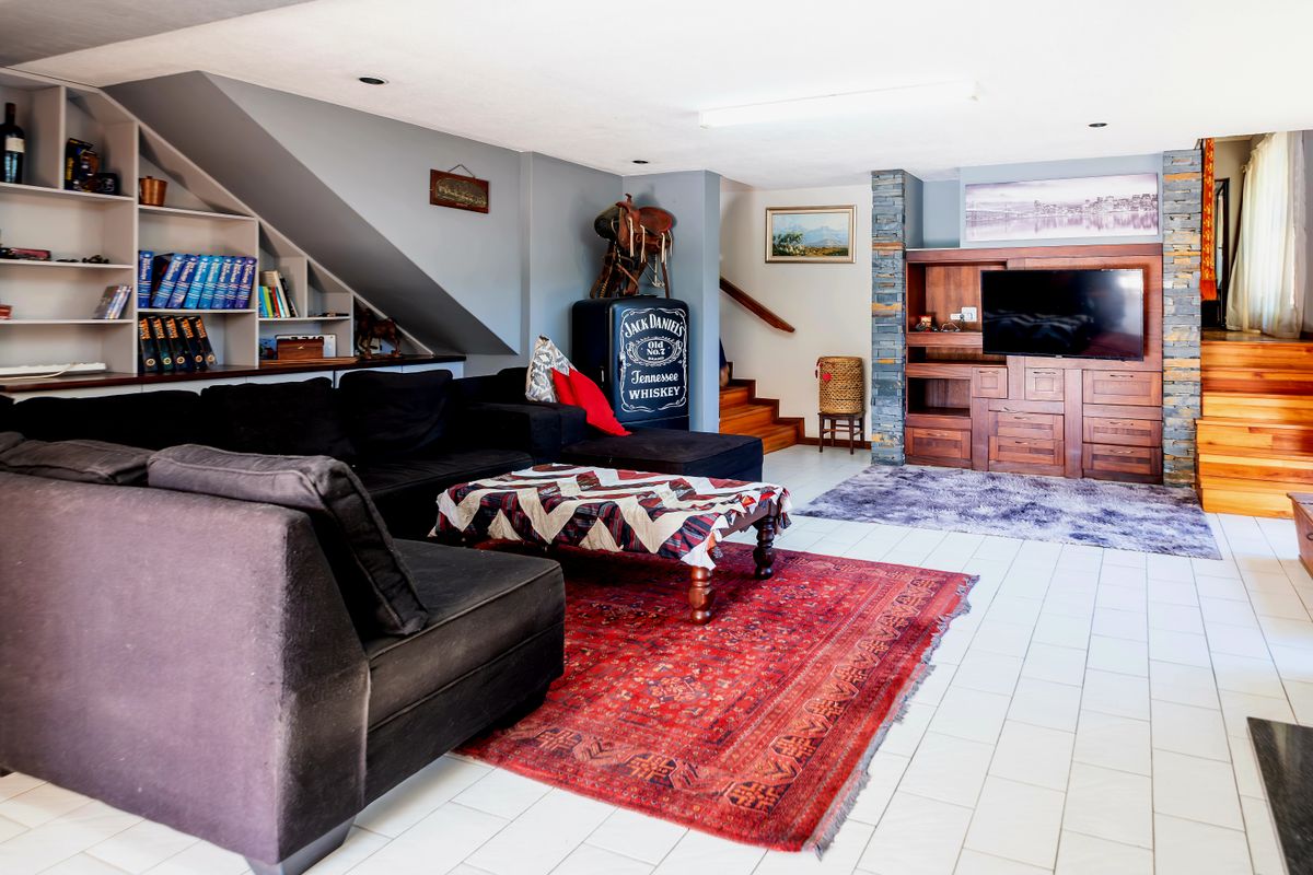 Spacious living room featuring built-in shelving, a stone-clad pillar, tiled flooring, and a wooden staircase leading to the upper level.