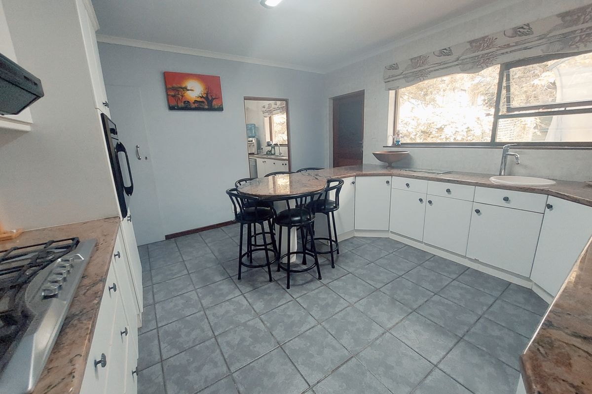 A functional kitchen featuring white cabinetry, granite countertops, a gas hob, built-in oven, and tiled flooring with an integrated breakfast nook area.