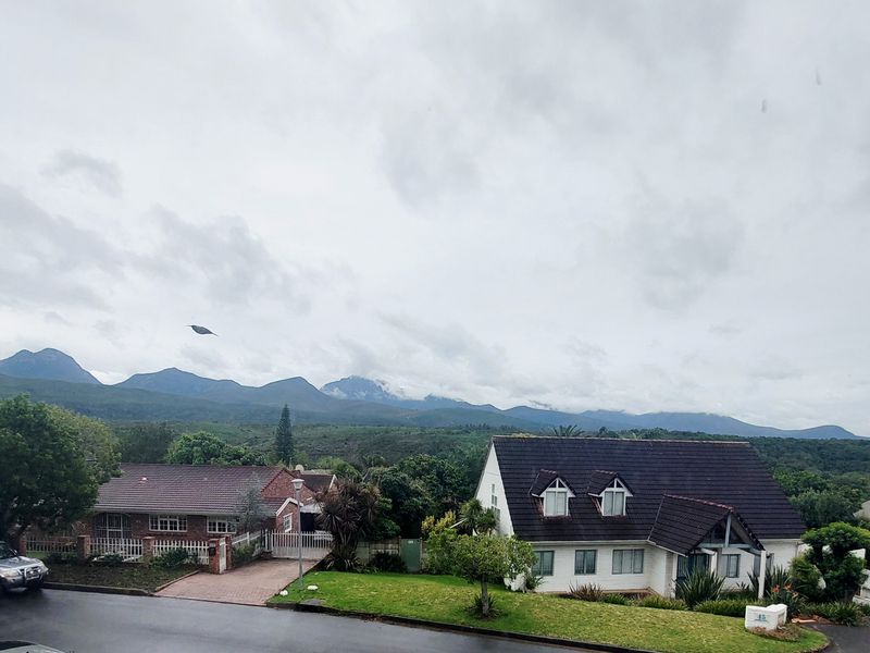 A scenic elevated view overlooking a residential neighbourhood with a prominent mountain range in the background under a cloudy sky.
