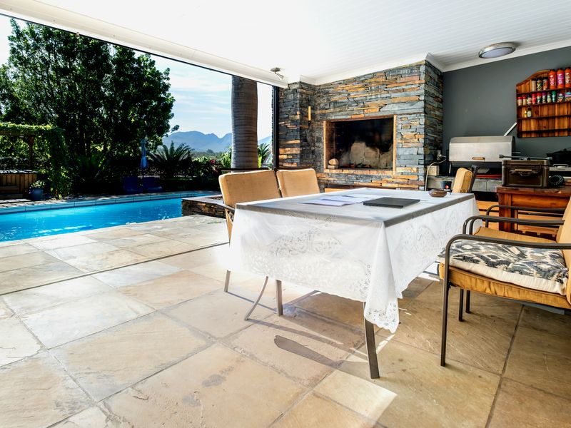 Covered outdoor patio featuring a built-in stone-clad braai, tiled flooring, and direct access to a swimming pool with mountain views.