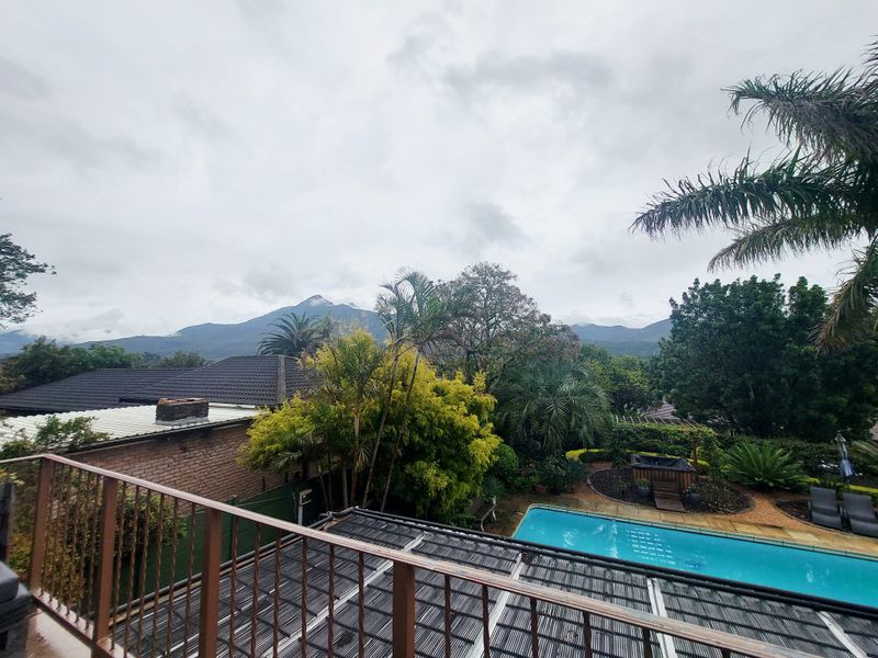 Elevated view overlooking a private swimming pool, landscaped garden, and surrounding residential area with scenic mountain views in the background.