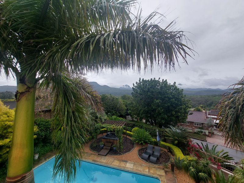 An elevated view of a private swimming pool, landscaped garden with a pergola, and scenic mountain views in the background.