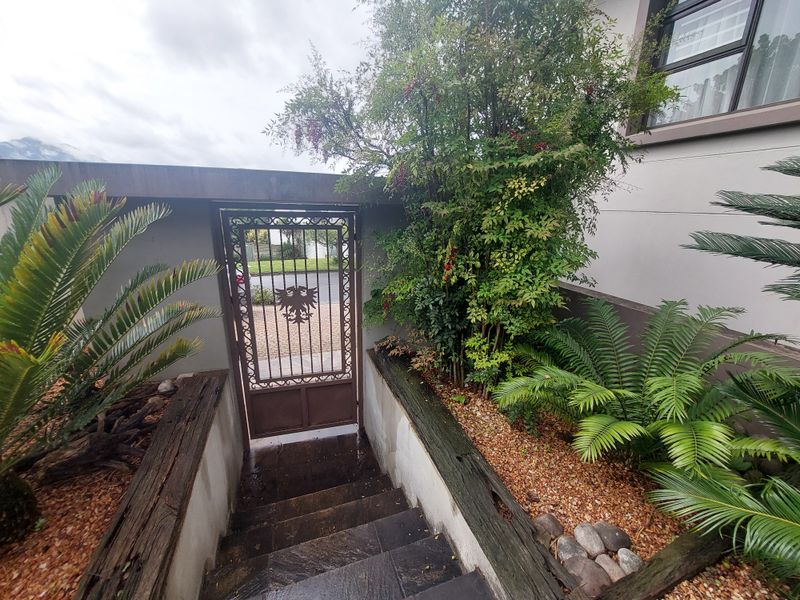 A gated entrance featuring stone steps leading down to a landscaped garden area with timber sleepers and a decorative wrought iron gate.