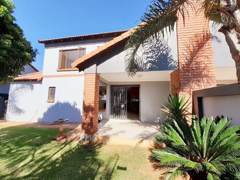 Rear view of the townhouse featuring a covered tiled patio, brick architectural detailing, and a well-maintained garden area.