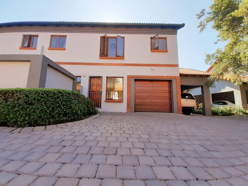 Front elevation of a two-story townhouse featuring a paved driveway, single garage, carport, and secure entrance.