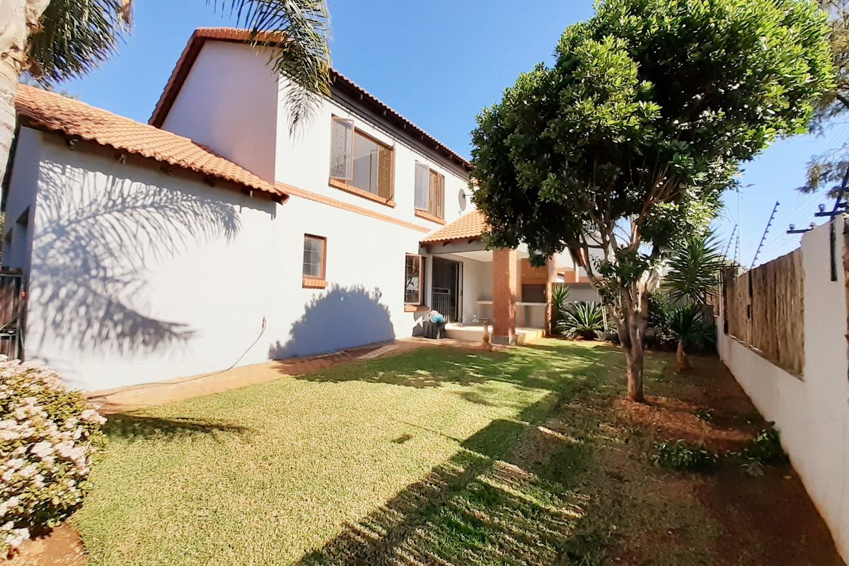 Rear view of the townhouse featuring a private garden, lawn area, and a covered patio with brick pillars under a terracotta tiled roof.