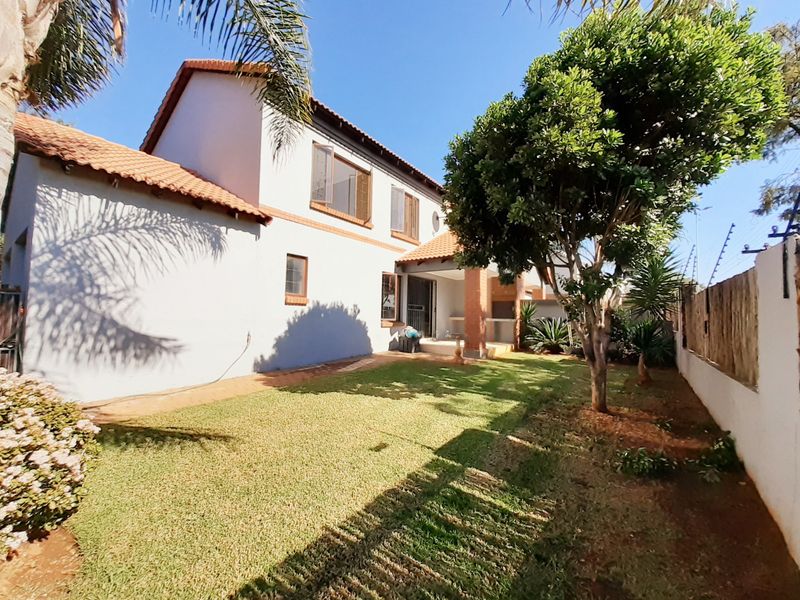Rear view of the townhouse featuring a private garden, lawn area, and a covered patio with brick pillars under a terracotta tiled roof.