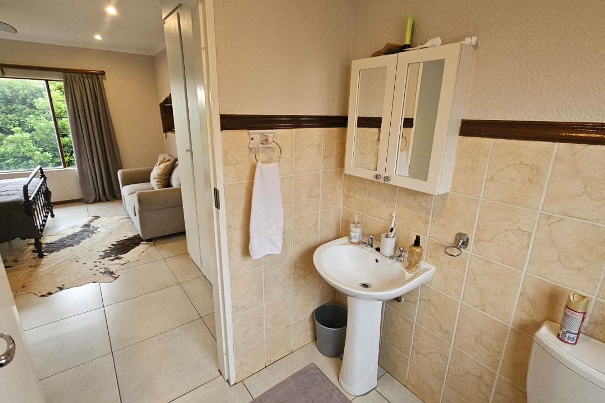 A functional bathroom featuring a pedestal basin, wall-mounted medicine cabinet, and neutral ceramic tiling, with an adjacent view into the bedroom area.