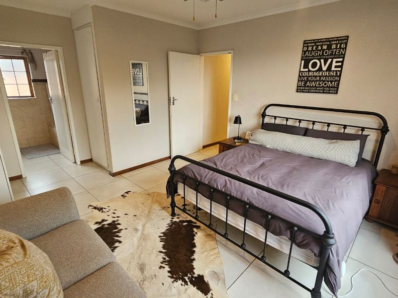 A spacious bedroom featuring tiled flooring, built-in cupboards, and direct access to an en-suite bathroom.