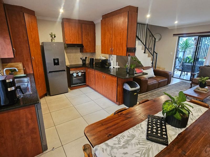 Open-plan living and kitchen area featuring wood-finish cabinetry, granite countertops, tiled flooring, and direct access to an outdoor patio via sliding doors.
