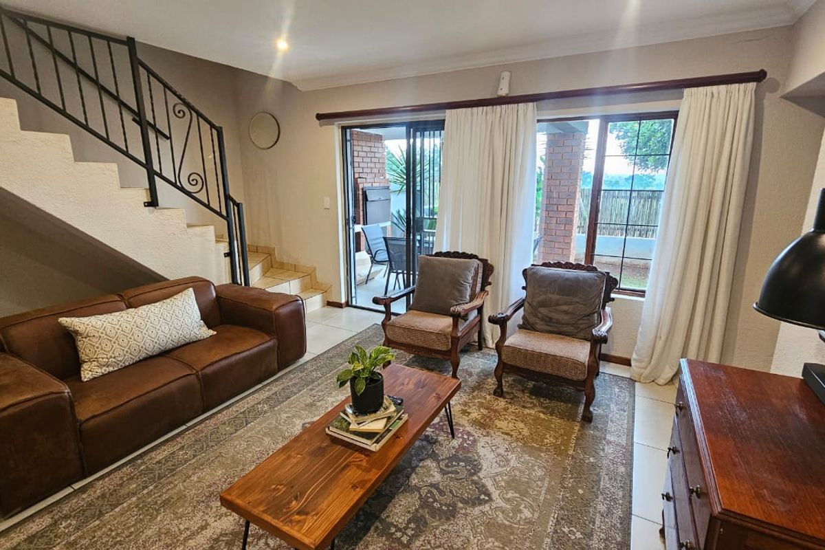 A comfortable living room featuring tiled floors, a staircase with a wrought iron balustrade, and sliding glass doors providing access to the patio.