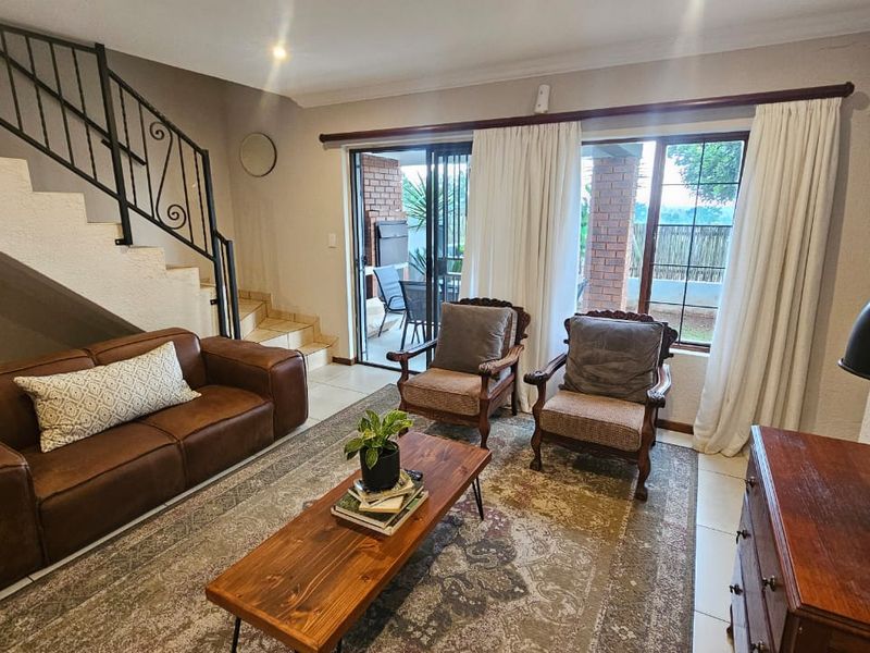 A comfortable living room featuring tiled floors, a staircase with a wrought iron balustrade, and sliding glass doors providing access to the patio.