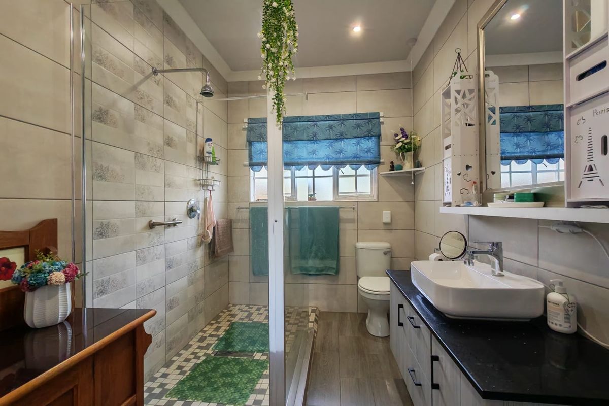 A modern bathroom featuring a walk-in shower with a glass screen, a sleek vanity with a countertop basin, and neutral wall tiling.