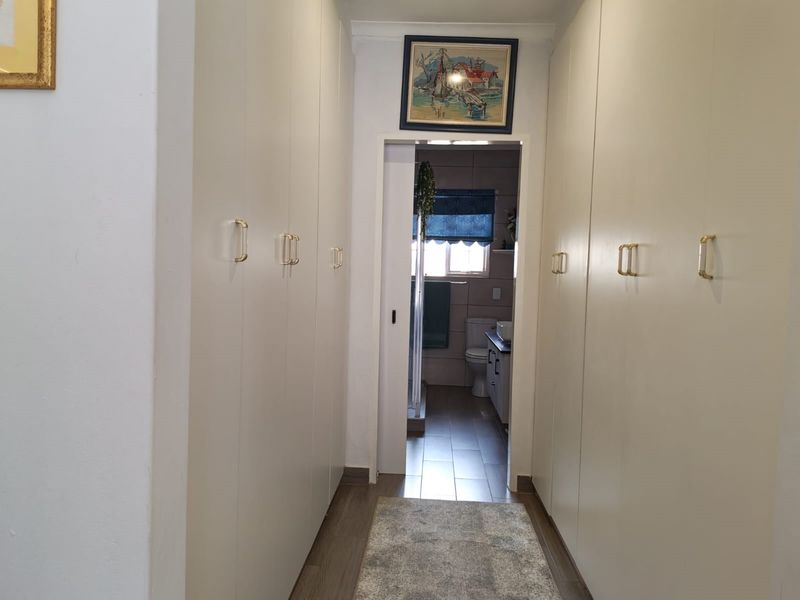 A functional hallway featuring extensive built-in storage cupboards with gold-tone handles, leading directly into a bathroom space.