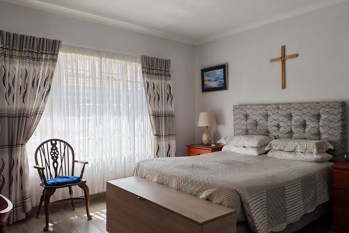 A well-maintained bedroom featuring tiled flooring and large windows with installed curtain tracks, providing a bright and comfortable living space.