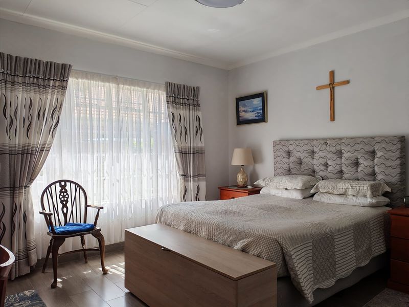 A well-maintained bedroom featuring tiled flooring and large windows with installed curtain tracks, providing a bright and comfortable living space.
