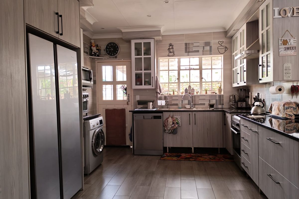 A functional kitchen featuring light wood-grain cabinetry, dark countertops, a tiled backsplash, and integrated appliances, offering a clean and well-maintained workspace.
