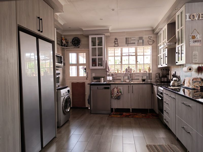 A functional kitchen featuring light wood-grain cabinetry, dark countertops, a tiled backsplash, and integrated appliances, offering a clean and well-maintained workspace.