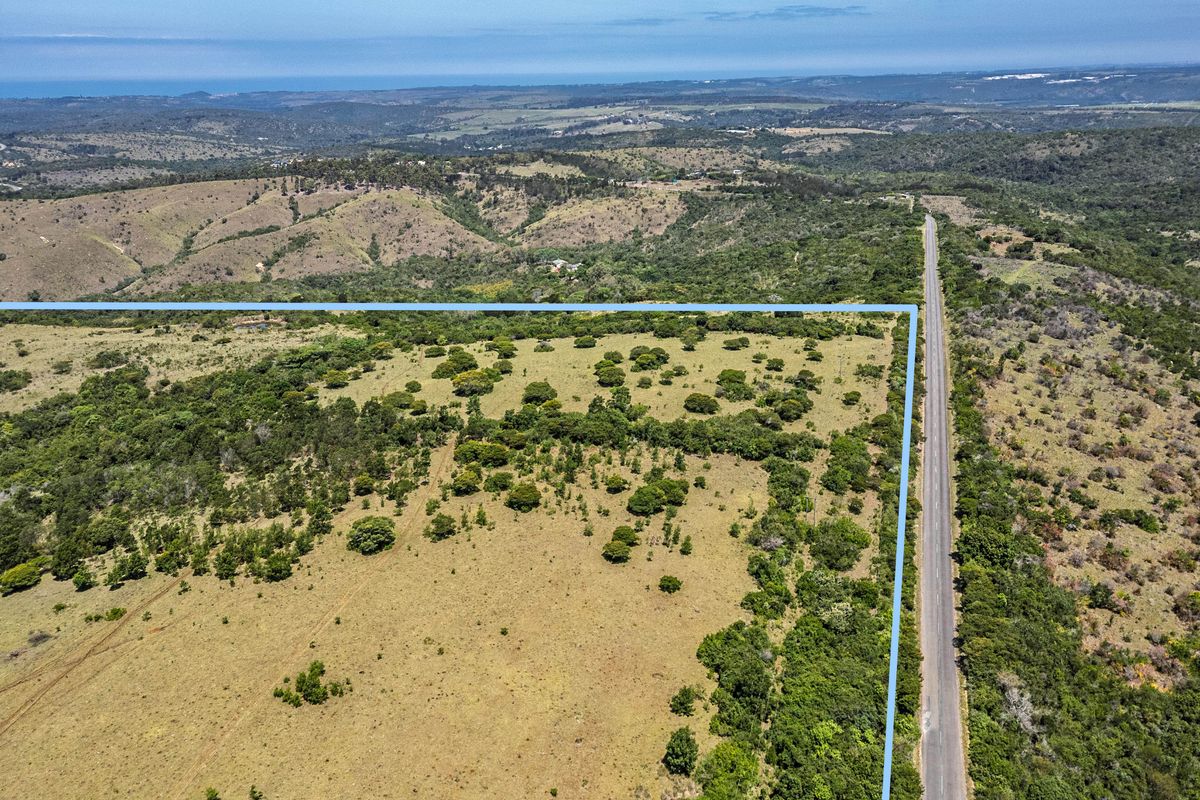 Aerial view of a large, open farm property featuring expansive natural landscape and direct access to a paved road.