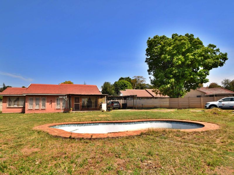 Rear view of the property featuring a swimming pool, tiled roof house, and a spacious garden area with boundary walling.