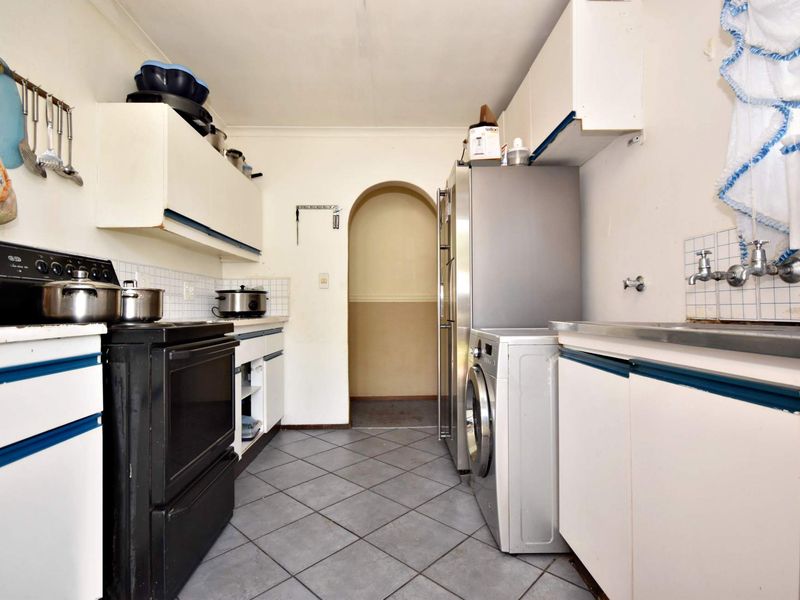 A dated kitchen featuring tiled flooring, built-in cabinetry, and a tiled backsplash, leading through an archway to an adjacent area.