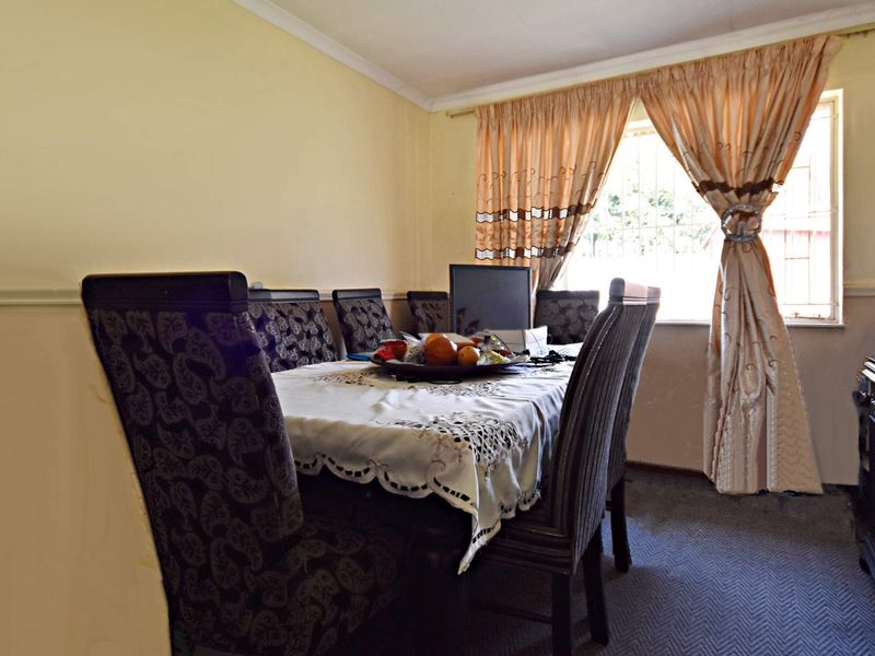 A functional dining room featuring carpeted flooring, a window with security bars, and coved ceiling detailing.