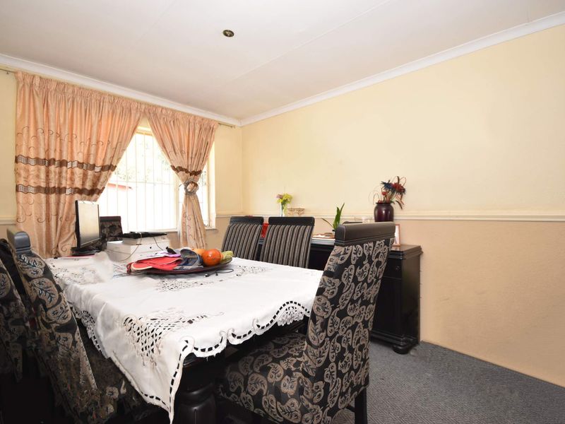 A dining room featuring carpeted flooring, coving, and a window fitted with security bars, offering a functional space for family meals.