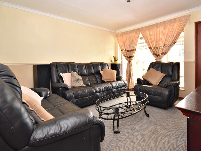 A living room featuring carpeted flooring, coved ceilings, and a window fitted with security bars, offering a functional space with potential for cosmetic updates.
