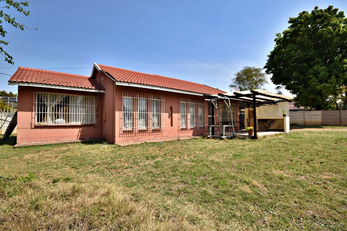 Rear view of the house featuring a tiled roof, security bars on windows, and a covered patio area with a built-in braai.