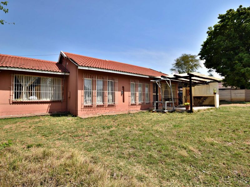 Rear view of the house featuring a tiled roof, security bars on windows, and a covered patio area with a built-in braai.
