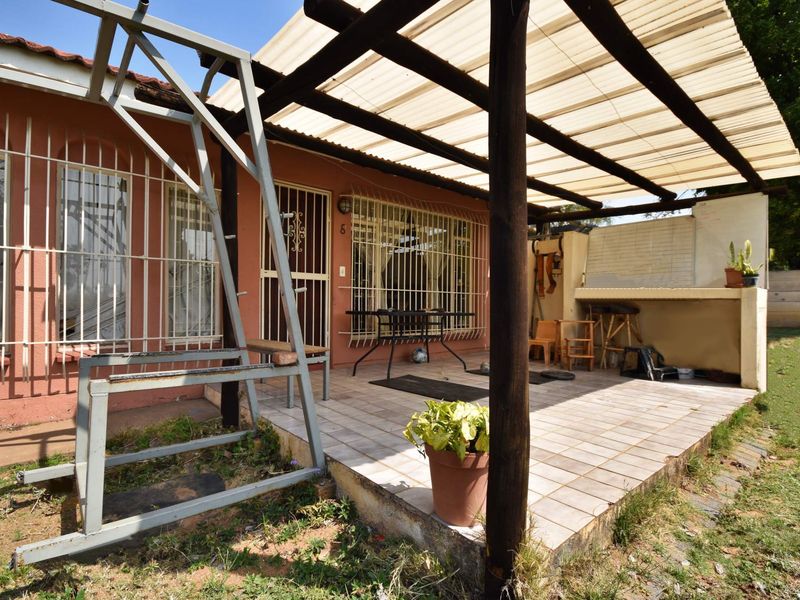 Covered outdoor patio area featuring a built-in braai, tiled flooring, and a timber pergola structure, providing a functional space for outdoor entertaining.