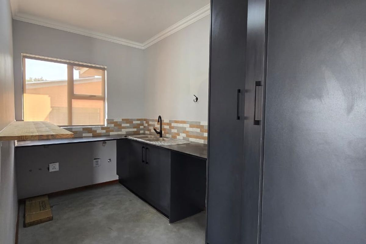 A modern, minimalist kitchen featuring dark cabinetry, a tiled backsplash, and polished concrete flooring, offering a clean and functional prep space.