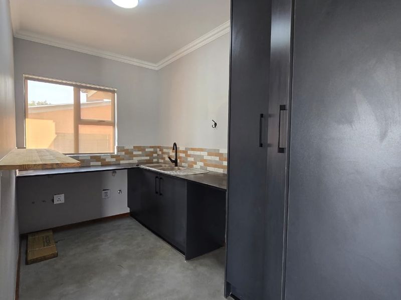 A modern, minimalist kitchen featuring dark cabinetry, a tiled backsplash, and polished concrete flooring, offering a clean and functional prep space.