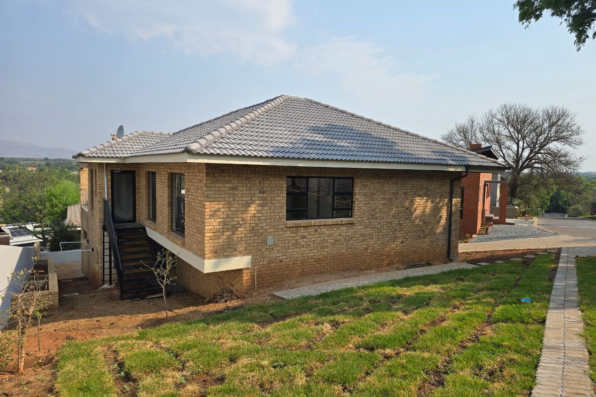 Rear view of a brick house featuring a tiled roof, metal staircase, and a paved walkway leading through the garden area.
